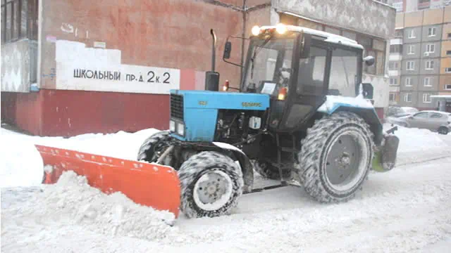 трактор убирает снег во дворе многоэтажки